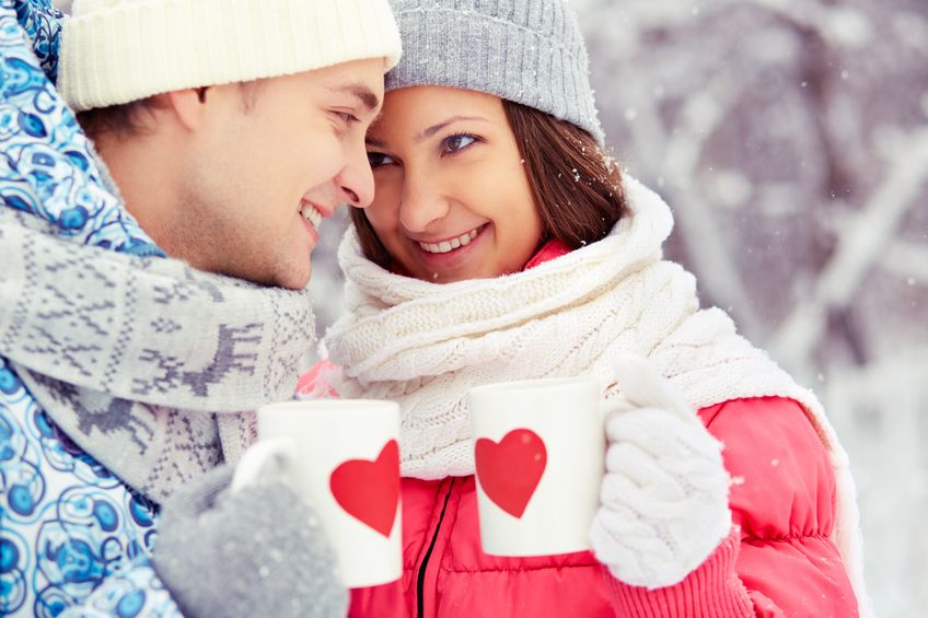 16964165 - portrait of happy young couple holding cups with red hearts in winter park